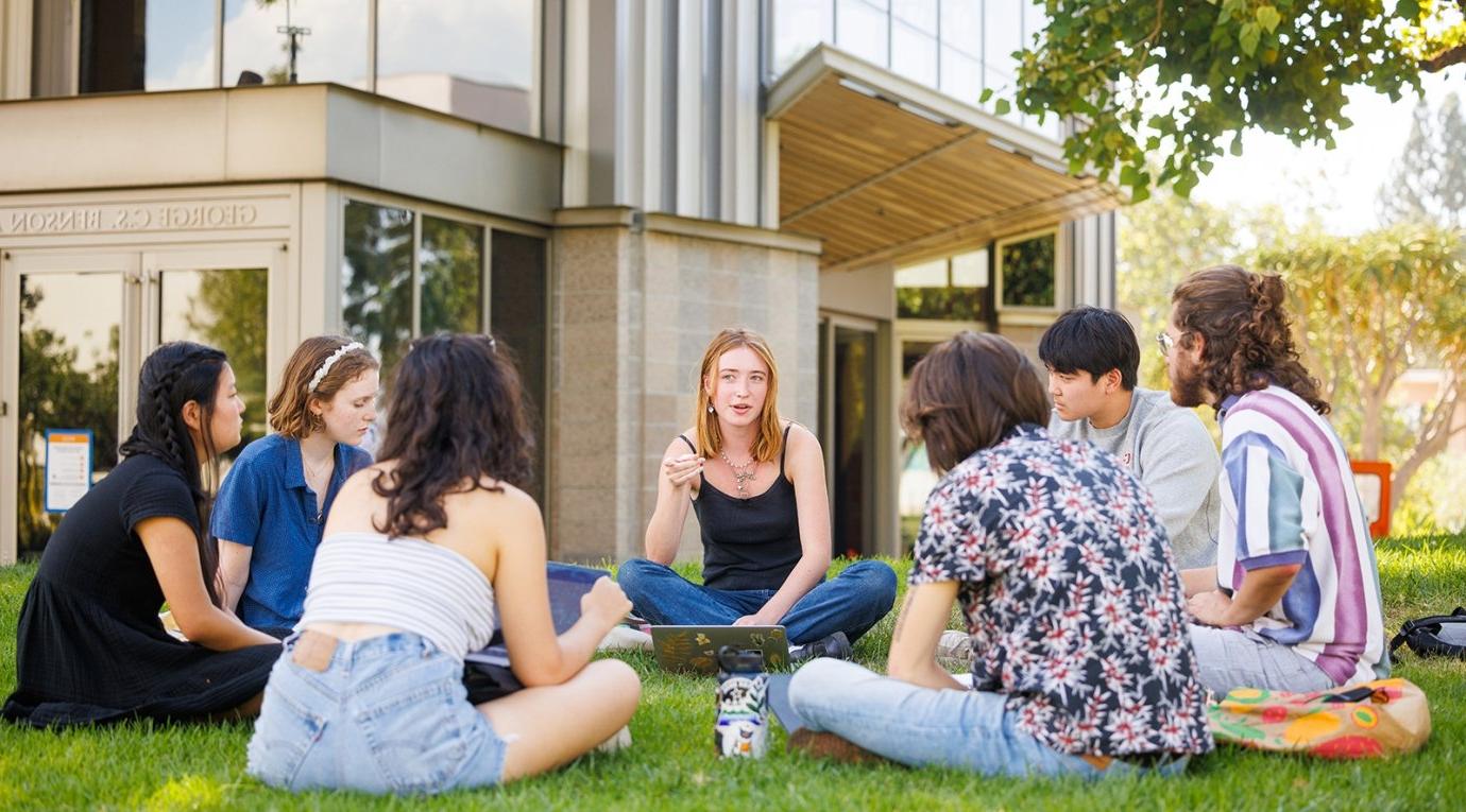 students sit on the grass in a cirle on the mounds during a study session